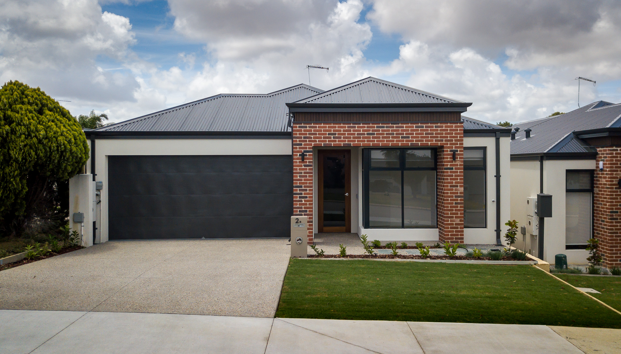 Front elevation of red brick SDA home with green grass and dark garage door