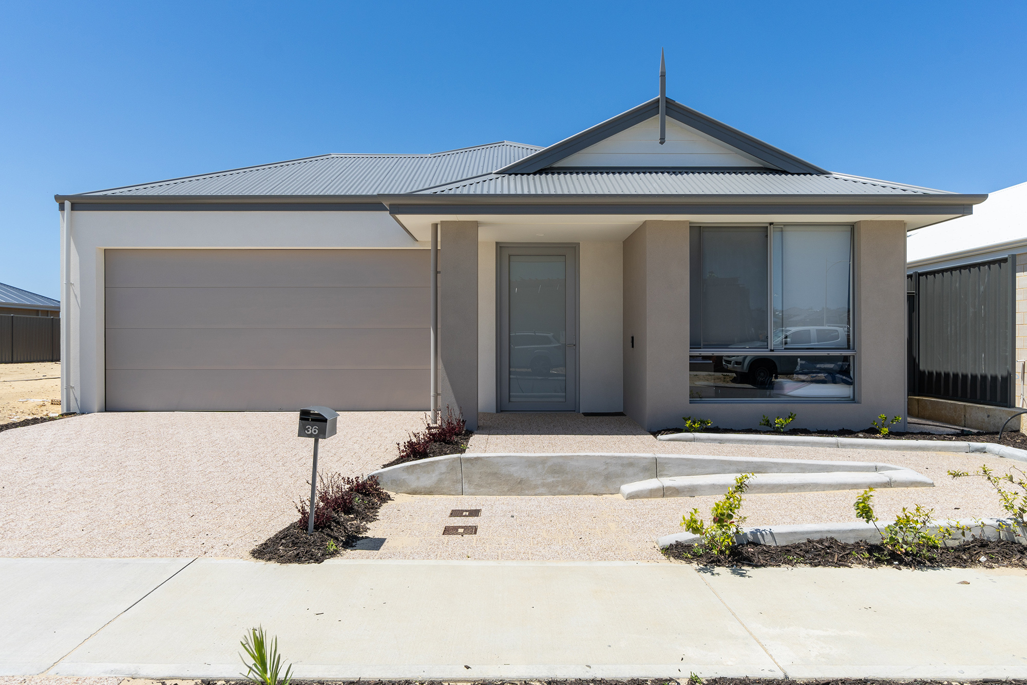 Front of a modern grey home with wide accessible driveway and ramp to front door including intercom and garden bed