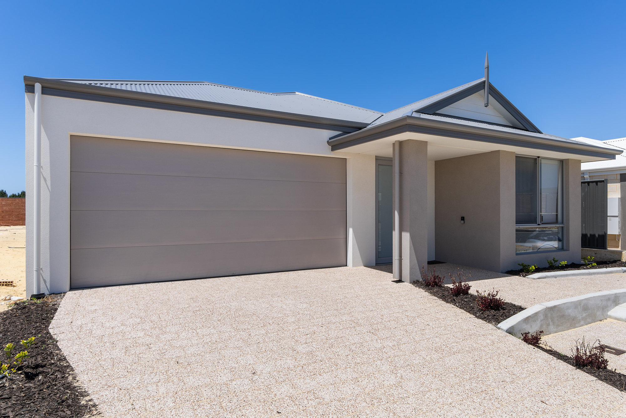 Front of a modern grey home with wide accessible driveway and ramp to front door including intercom and garden bed