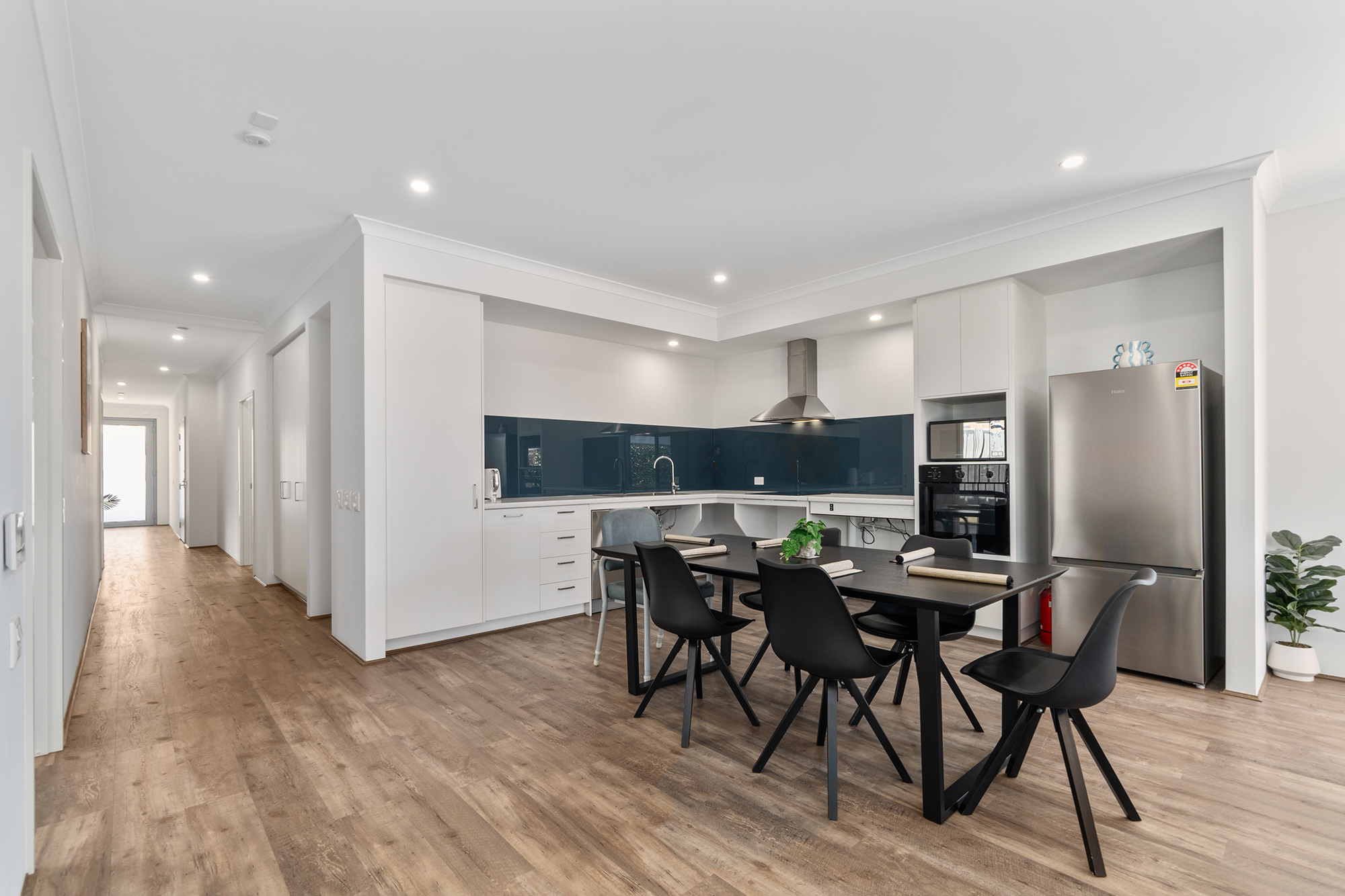 Light kitchen with navy splash back, adjustable height benchtop, double fridge and appliances. A black 6 set table setting for meals in the middle.