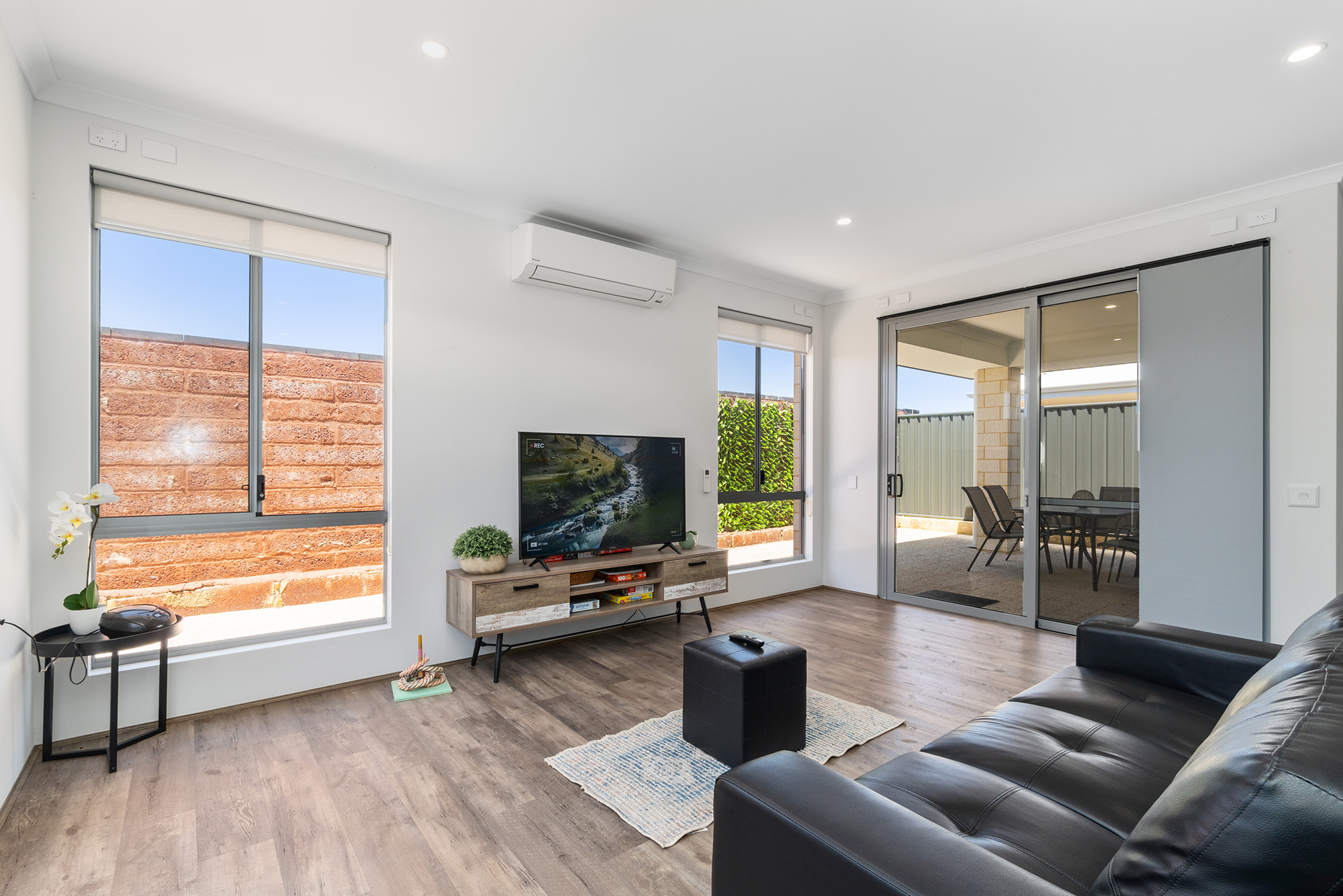 Light and bright loungeroom with sofa, tv, and boardgames overlooking a blue sky out onto the alresco.