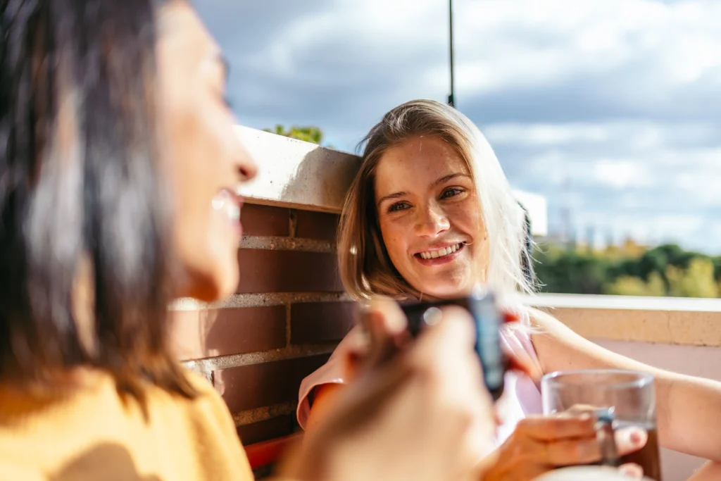 Young girl with blonde hair, cup of tea in hand, sitting with friend on balcony